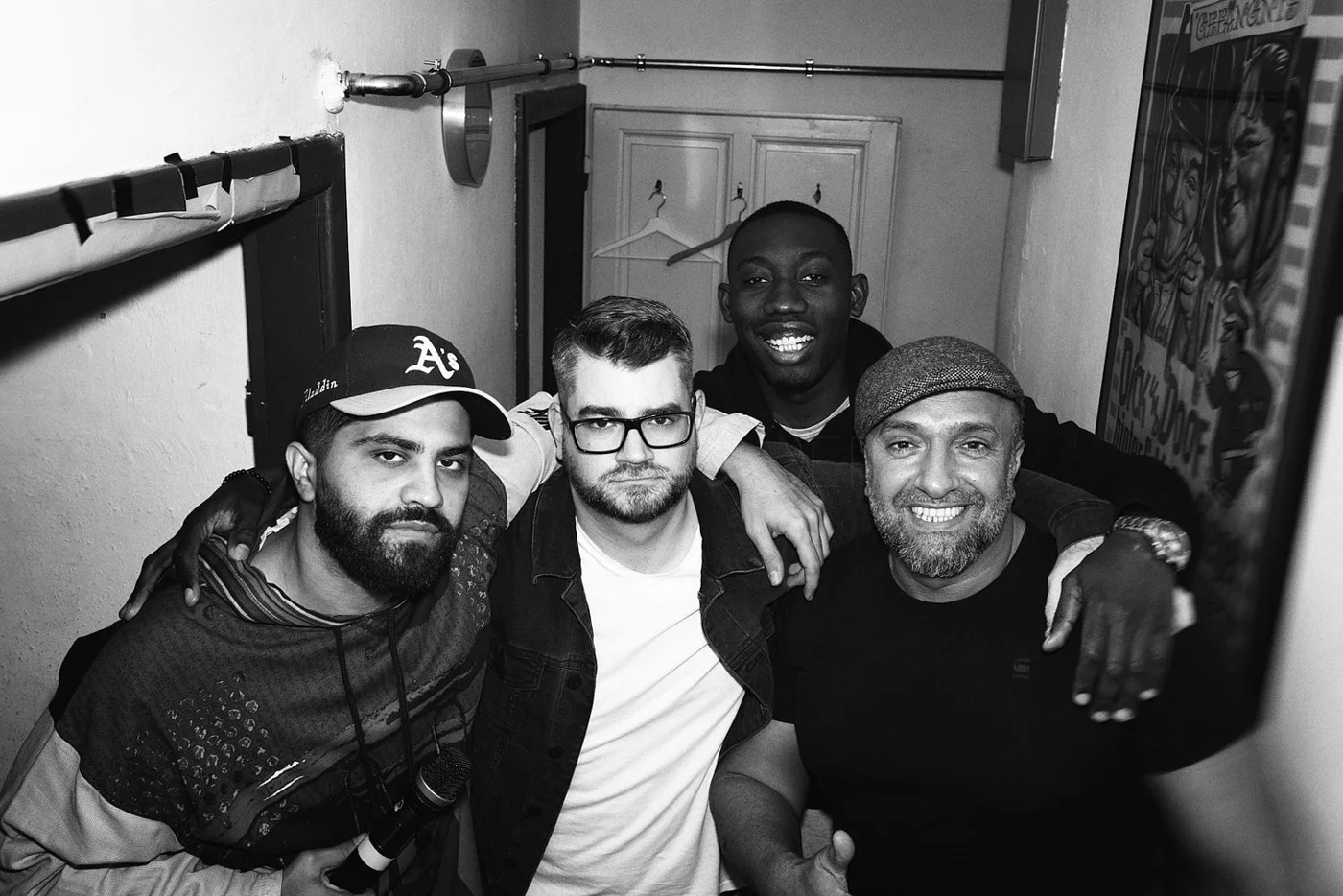 Four men posing together indoors in a black-and-white photo, smiling and embracing each other.