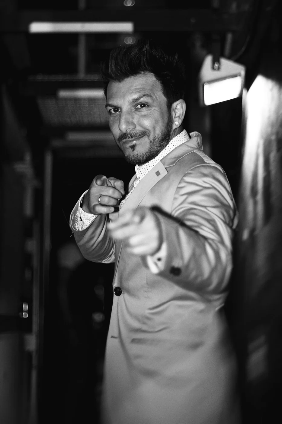 A man in a suit smiles and points at the camera, in a black-and-white photo.
