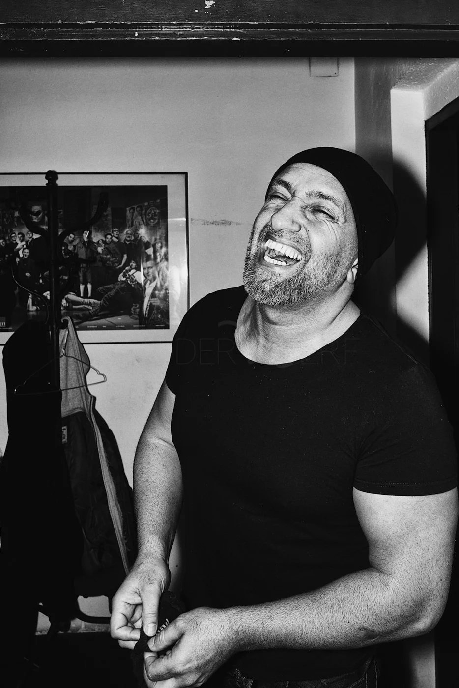 A man with a beard and mustache, wearing a black beanie and shirt, smiling and laughing.