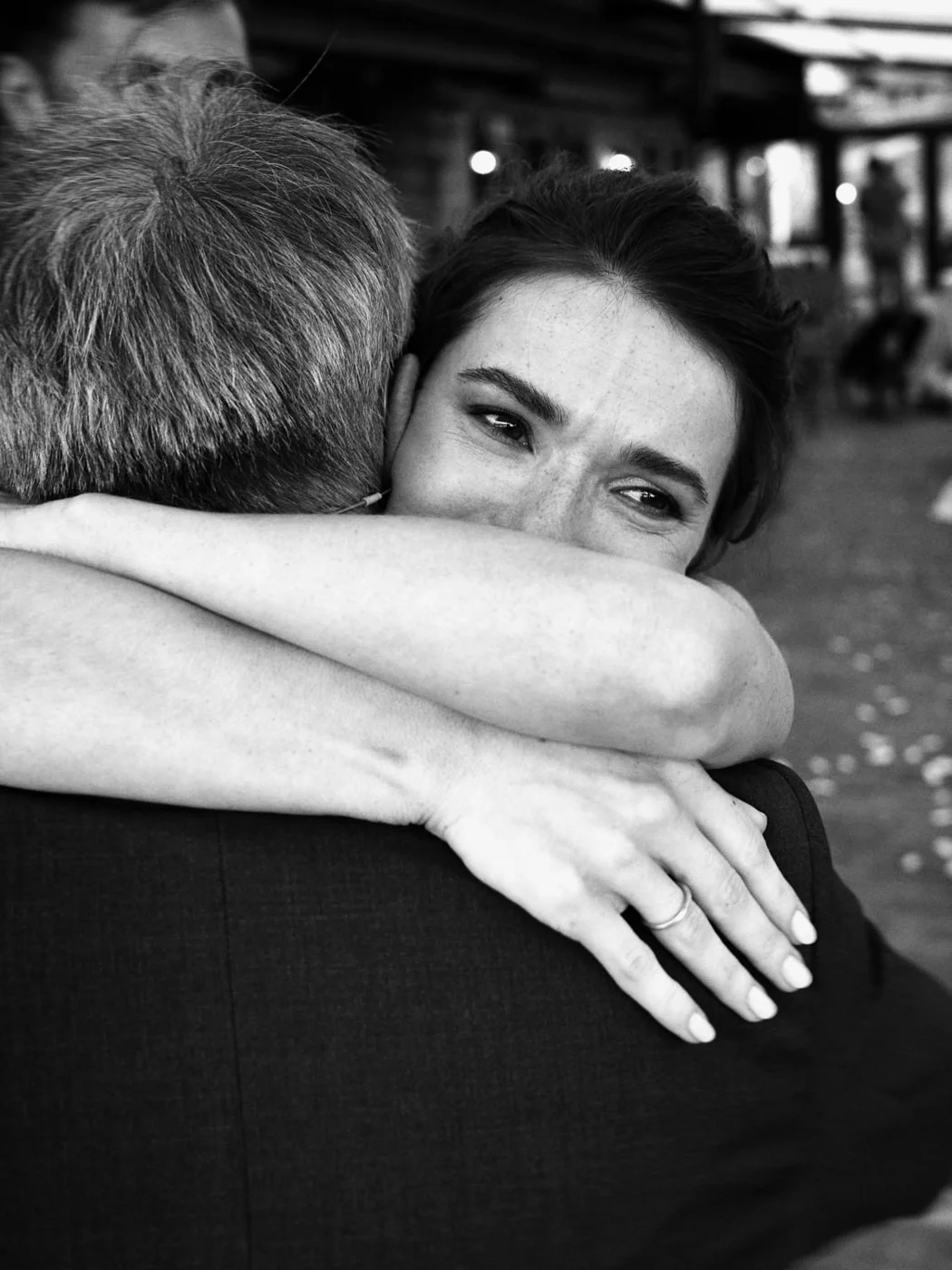 A black-and-white photo of a woman hugging a man. The woman has her eyes closed with a gentle smile and visible freckles, while the man has his face turned away from the camera.