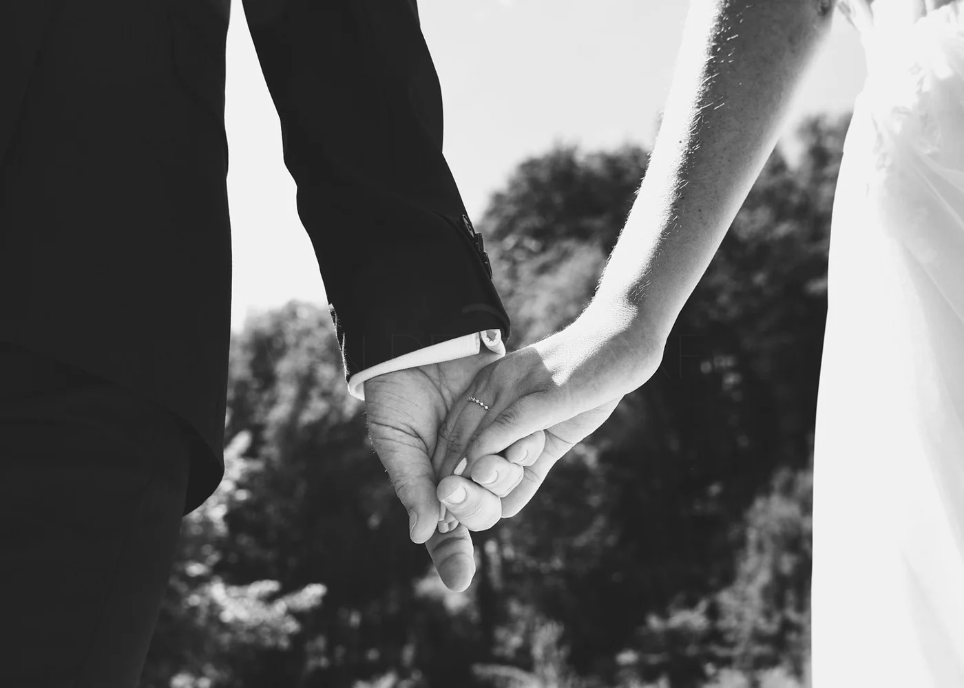 Close-up of a bride and groom holding hands outdoors, black and white photograph.