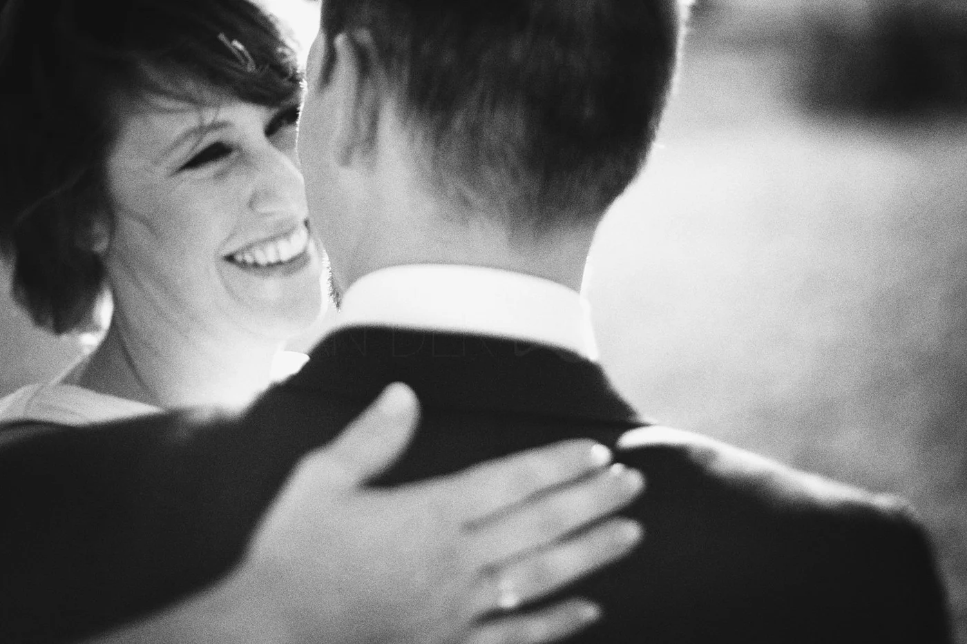 A woman with short hair smiling and embracing a man with short hair, viewed from behind, in a black and white photograph.