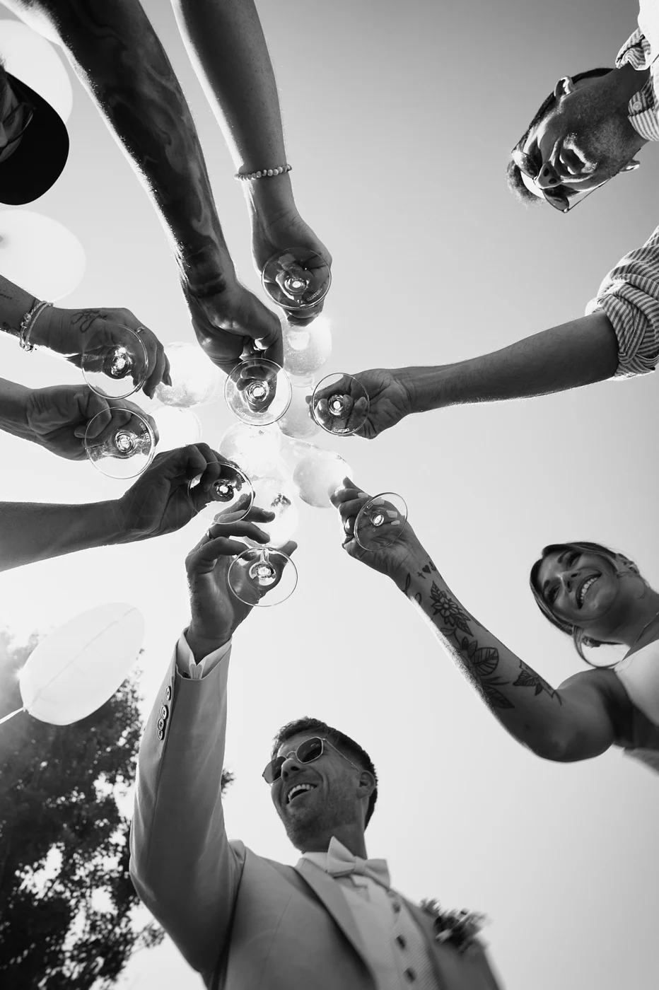 Group of friends raising glasses in a toast at an outdoor celebration, seen from below against a clear sky.