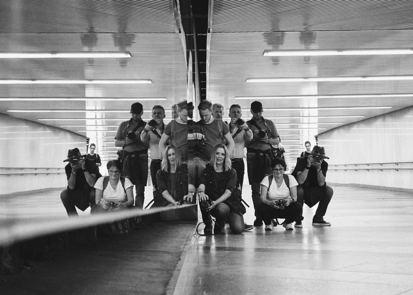 A group of people taking a photo in a reflective tunnel with a mirrored wall, black and white photo