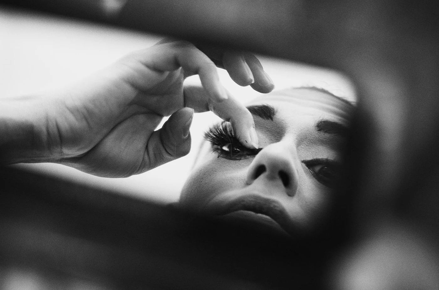 Close-up of a woman applying eye makeup, reflected in a mirror, in black and white.