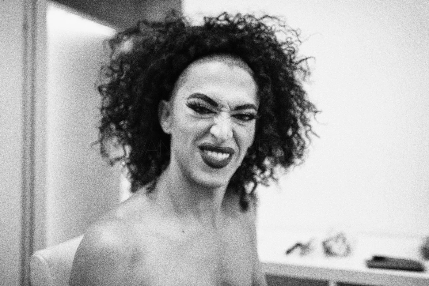 Black and white photo of a woman with curly hair making a grimace or playful expression.