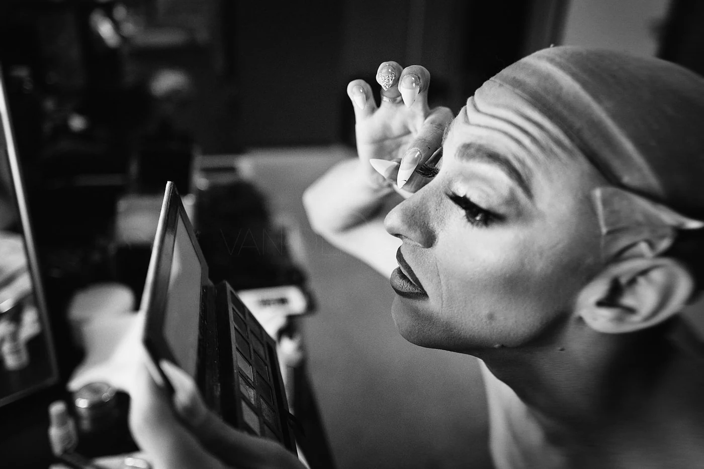 A woman applying eyeshadow in front of a mirror, with makeup tools and cosmetics nearby.