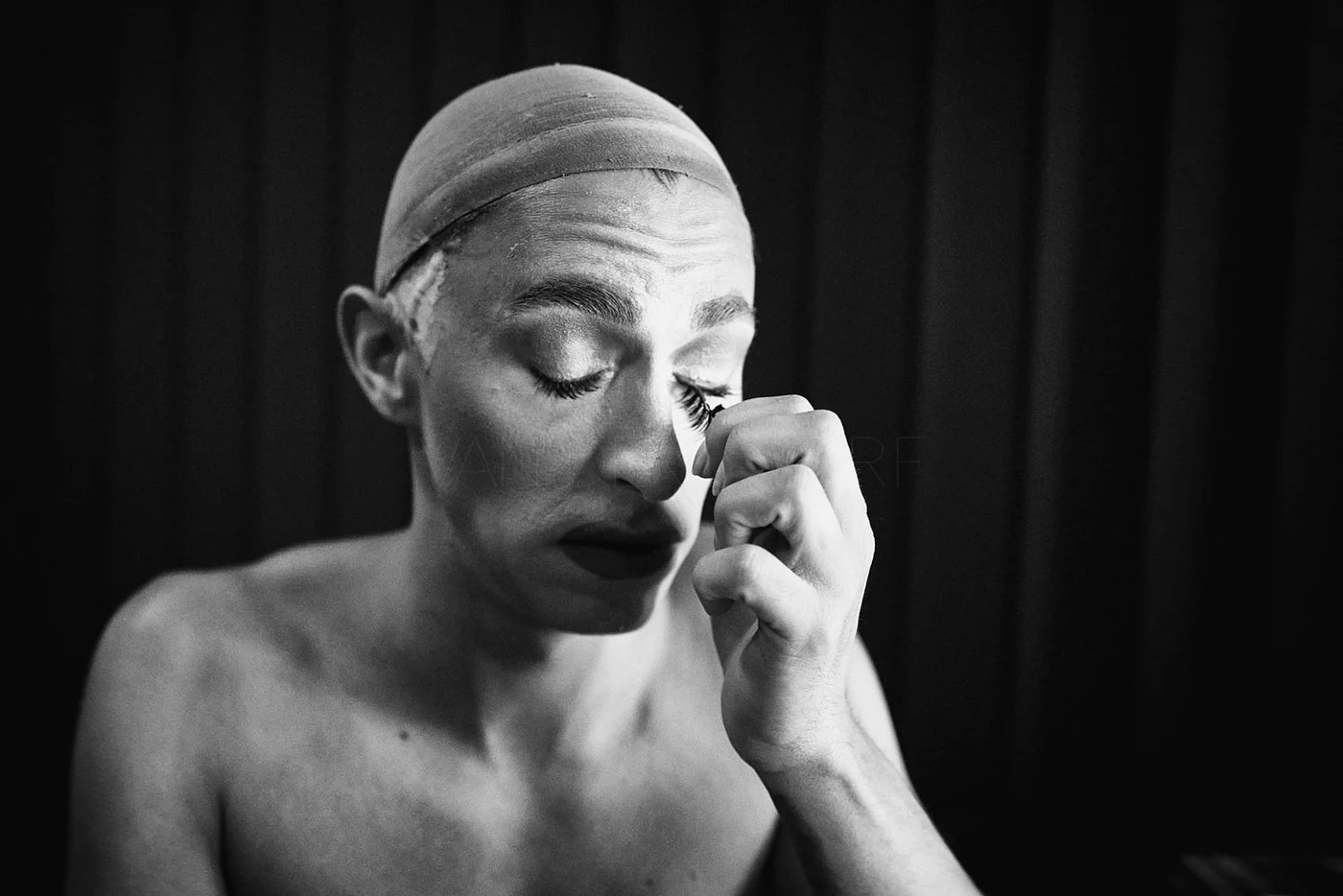 A woman with a bandana on her head, closed eyes, and dark lipstick, holding her hand near her eye, with her fingers touching her eyelashes, in a black and white portrait photo.