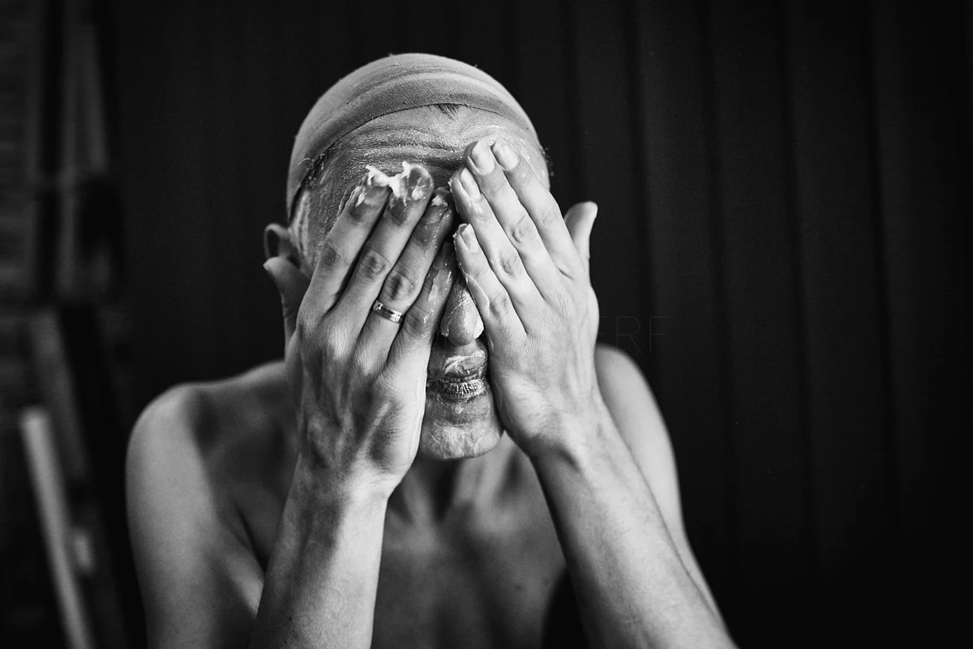 A woman washing her face with soap, covering her face with her hands, in black and white.