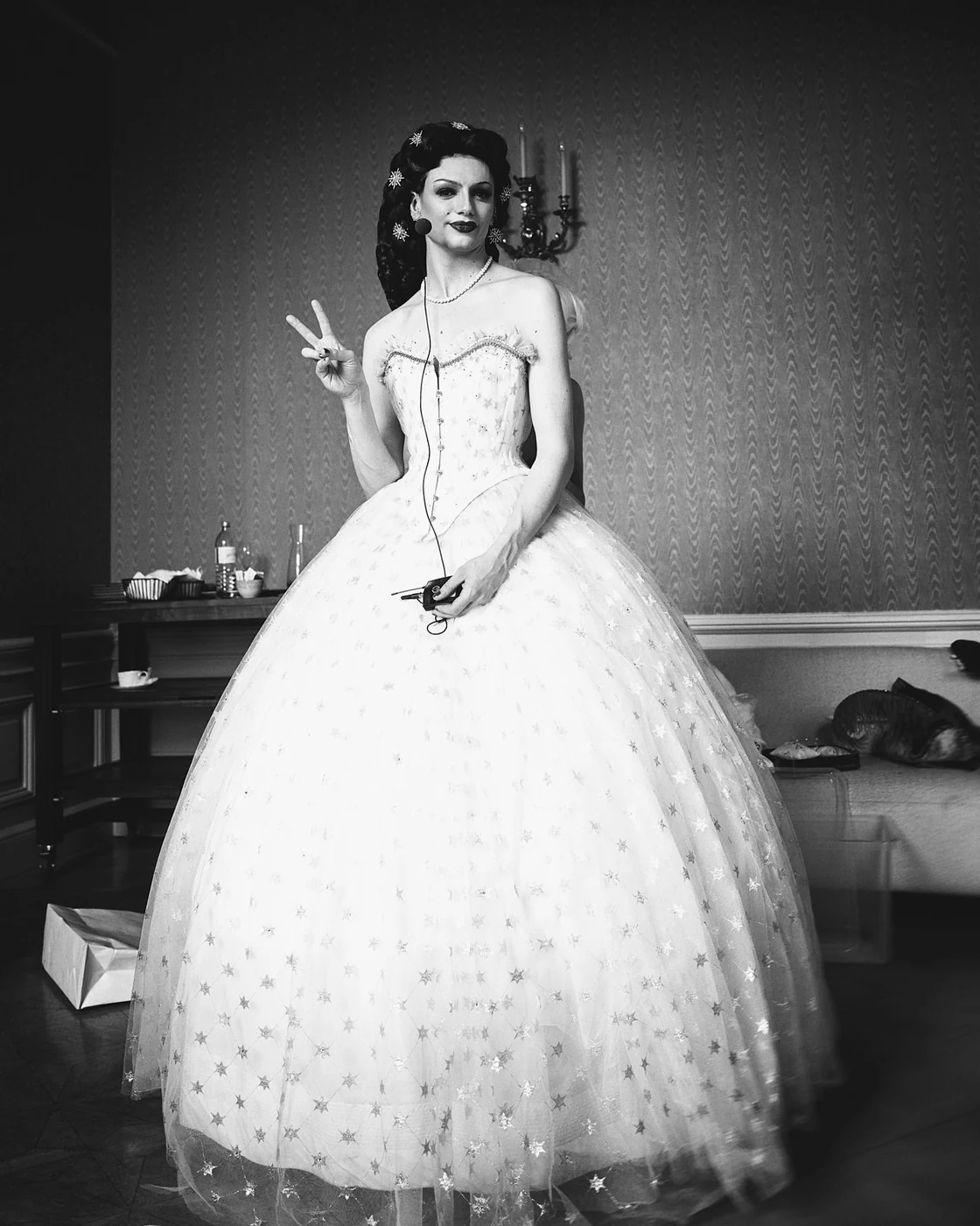 A woman dressed like a princess in a ball gown posing and making a peace sign gesture.