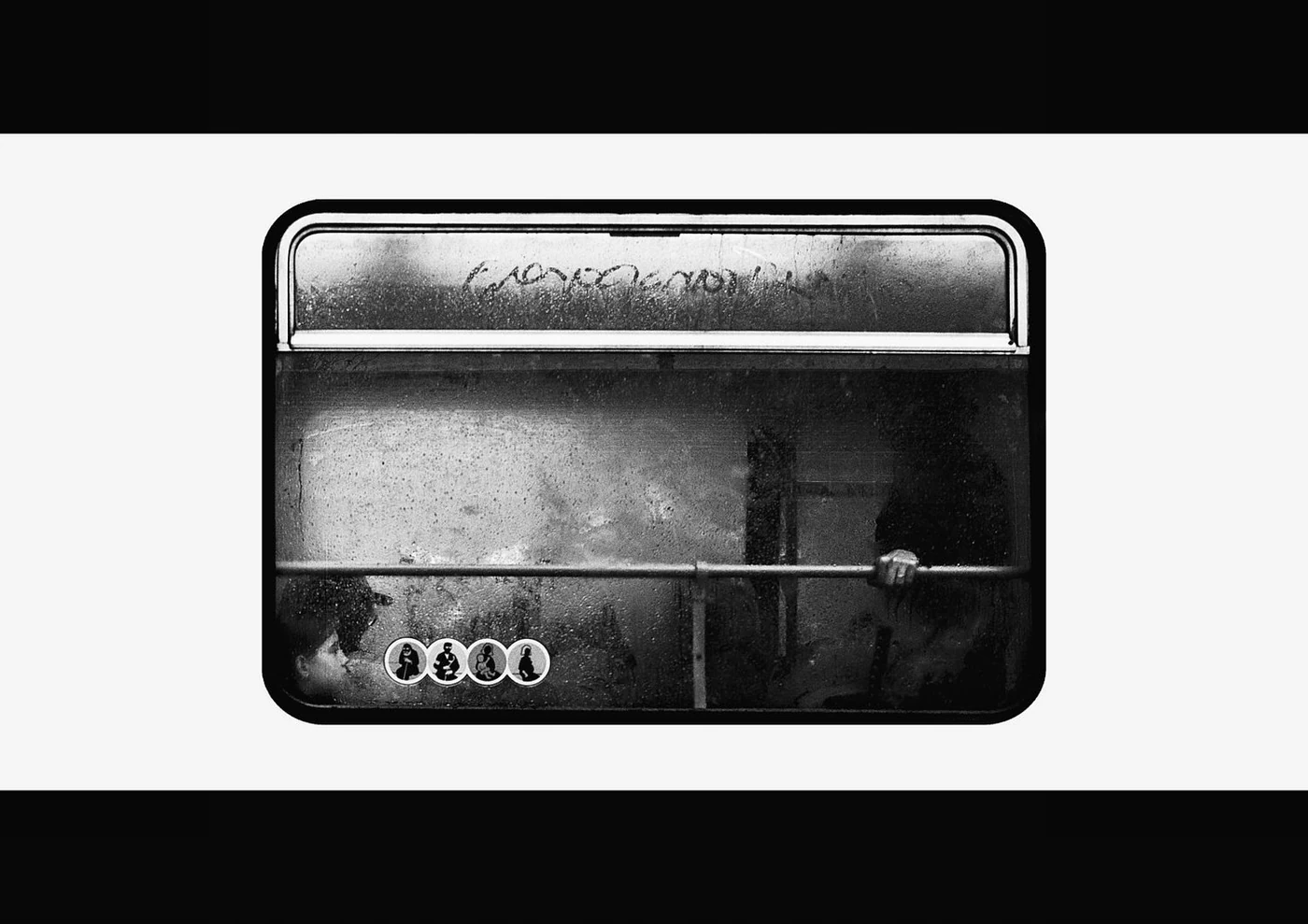 Black and white photo of a foggy, empty bus window with four stickers of children in safety seats at the bottom left corner.