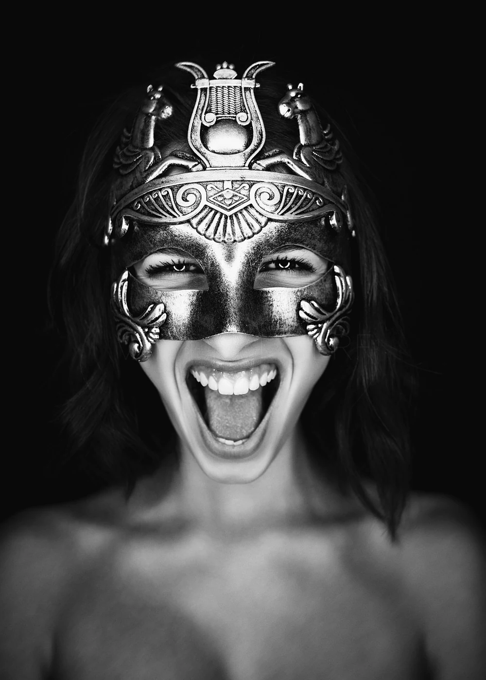 A woman wearing an ornate, metallic mask with open mouth and eyes expressing joy or excitement, black background.