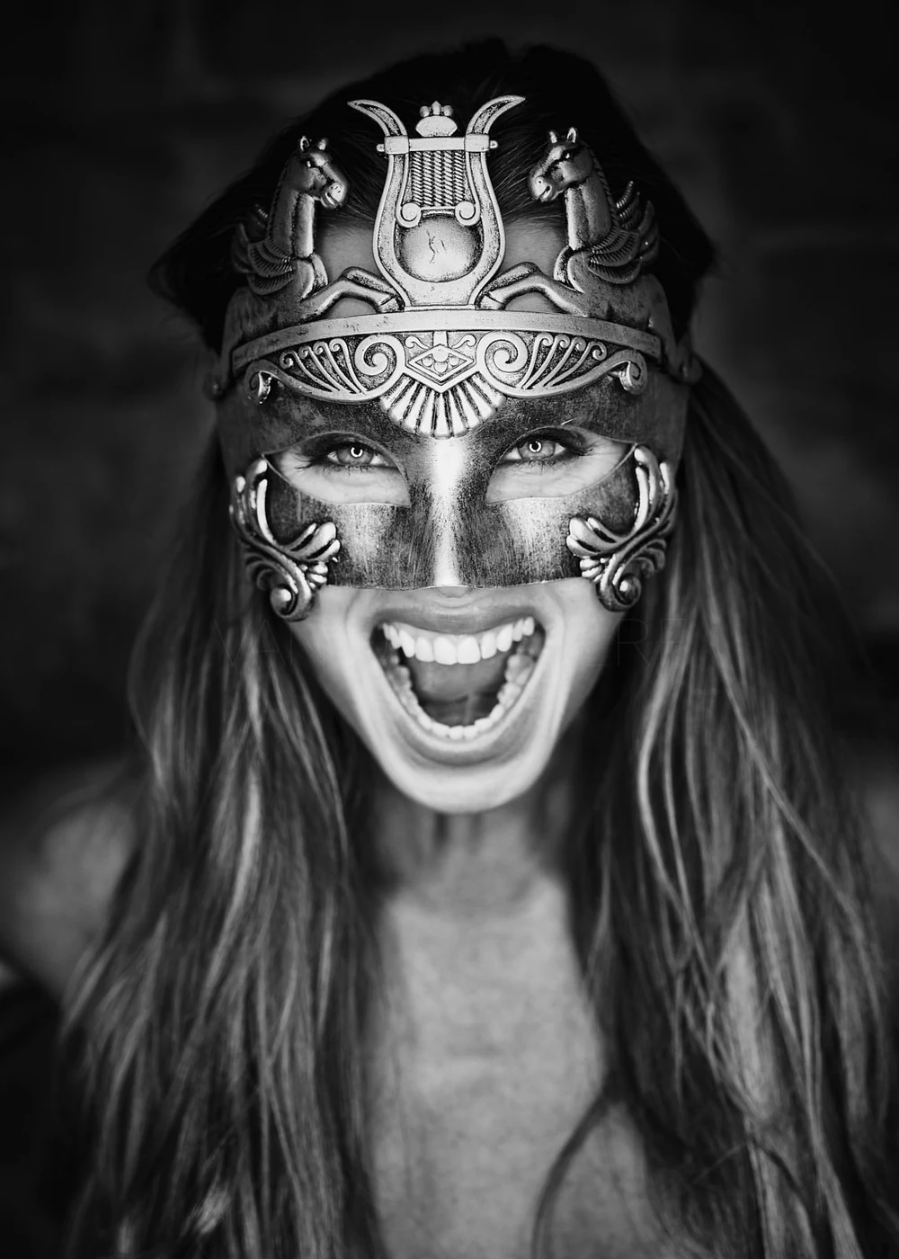 A woman with long hair wearing an ornate Viking-style mask with horse and dragon motifs, showing her smiling with her mouth open.