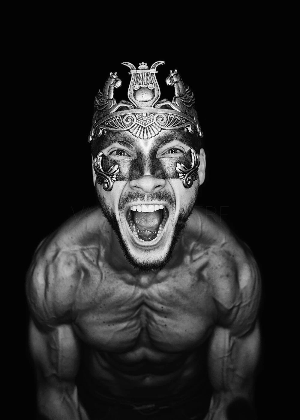 A muscular man with an open mouth, wearing an ornate metallic mask and a headdress with horse figures, against a black background.