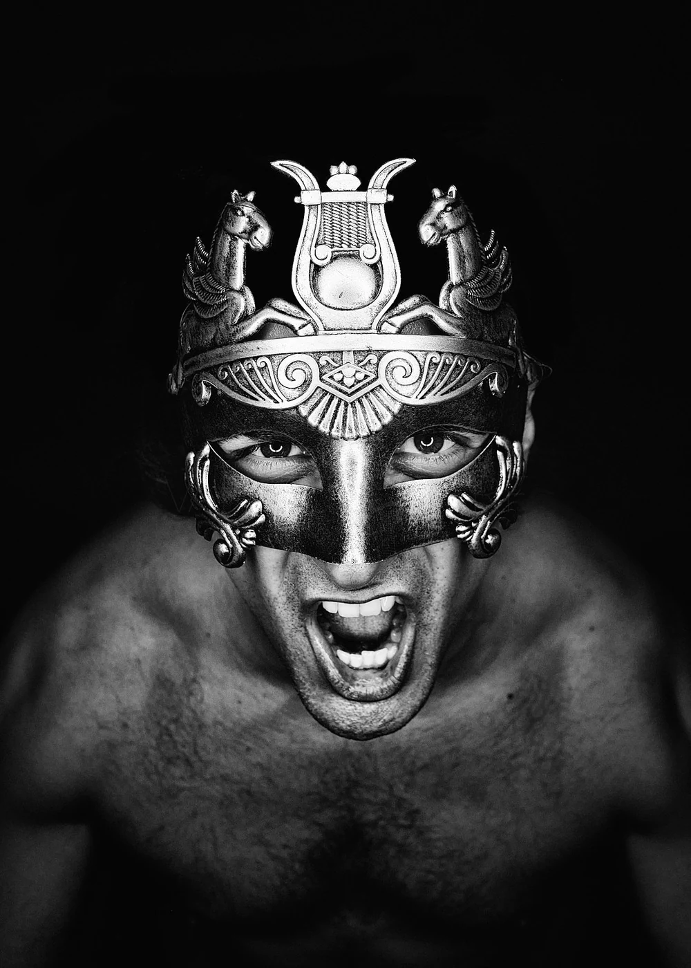 A person wearing an ornate mask with two horses and a crown, shouting aggressively against a dark background.