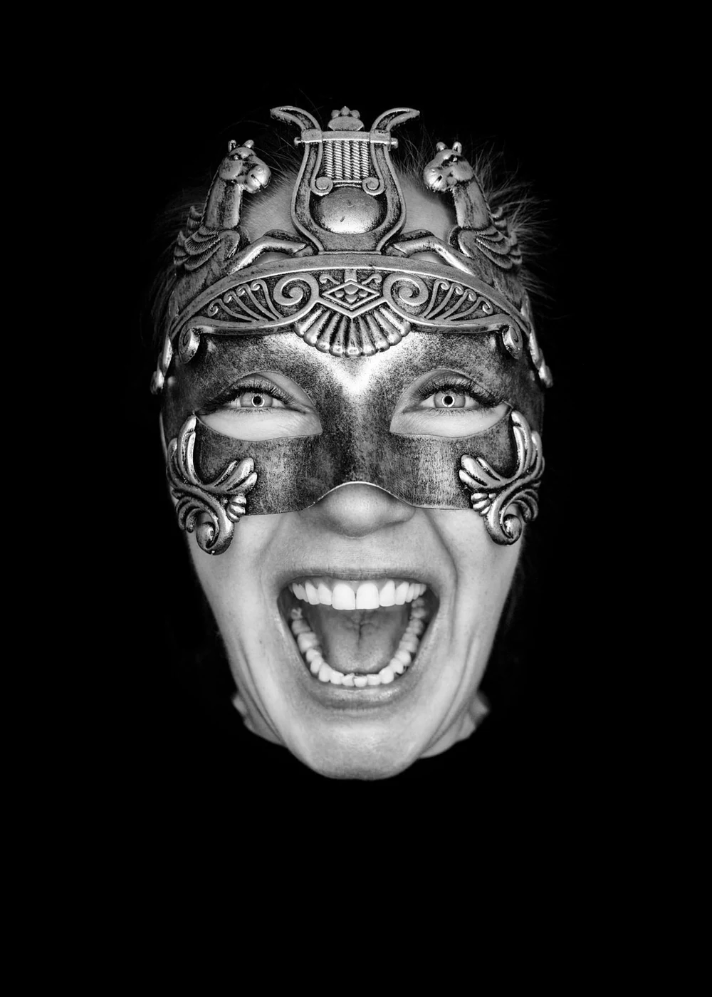 Person wearing an ornate metallic mask with open mouth expressing excitement, black background.