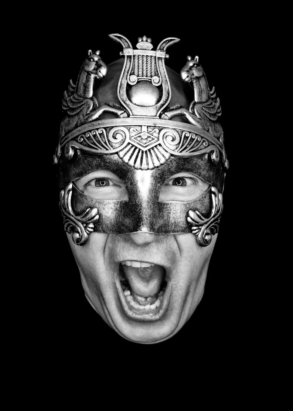 Black and white photo of a person wearing a decorative, ornate mask with an open mouth, revealing teeth, and eyes visible through eye holes.