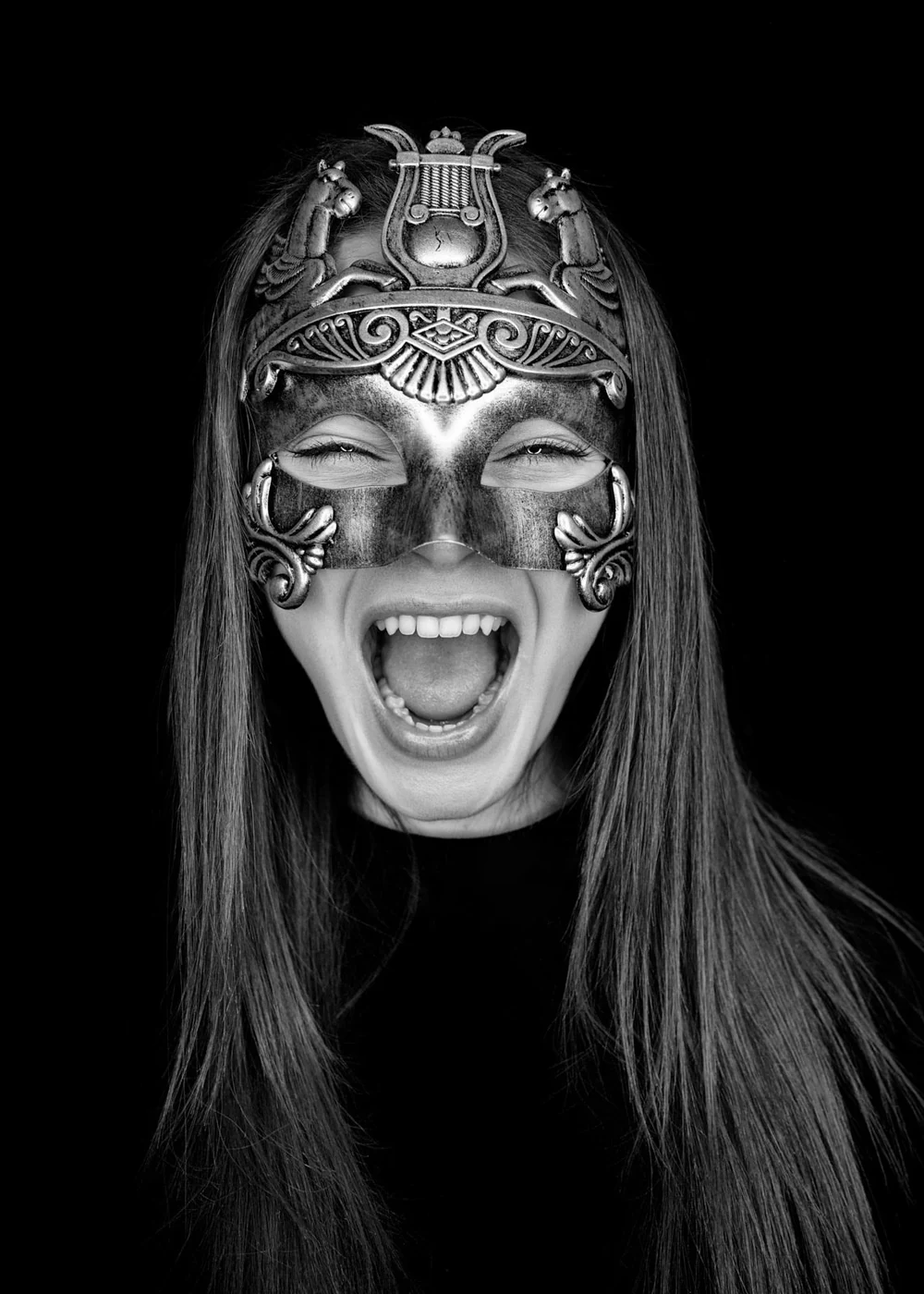 Black and white photo of a woman wearing an ornate, decorative mask with an expression of excitement or joy.